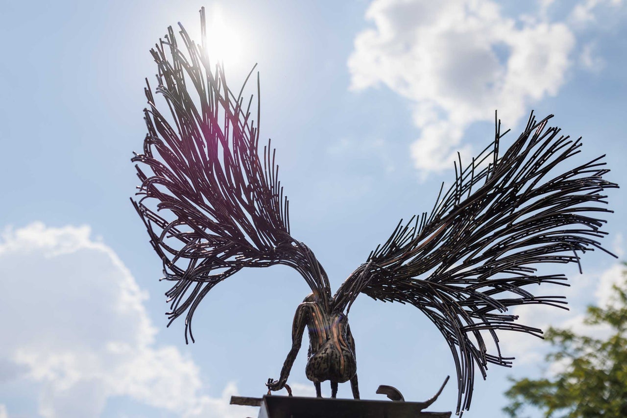 Sculptură a unei figuri înaripate din metal pe un fundal de cer înnorat