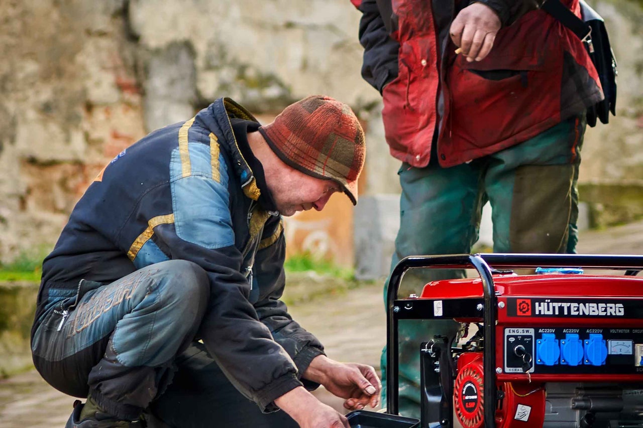 Un meșter întreține un generator de curent Hüttenberg în exterior, în timp ce o a doua persoană stă alături.