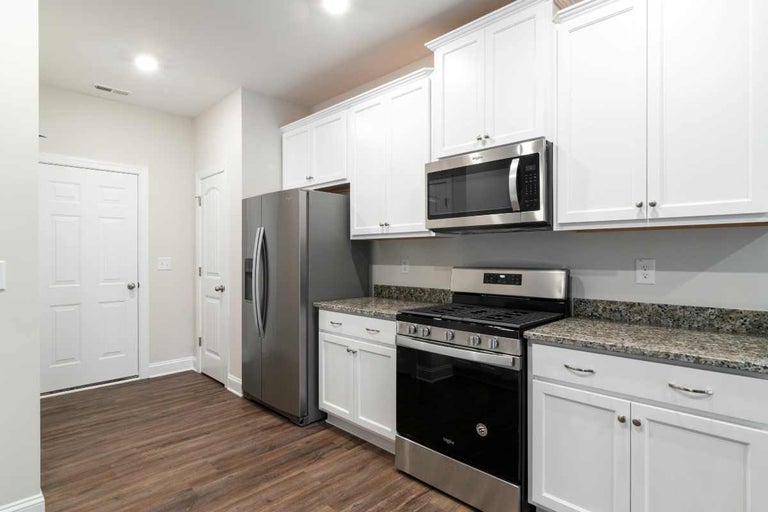 Bucătărie modernă cu dulapuri albe, blat de granit și aparate din oțel inoxidabil pe o pardoseală laminată cu aspect de lemn închis.