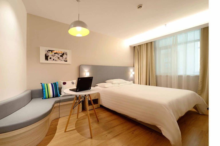 Cameră luminoasă de hotel cu pat, zonă de relaxare, masă și laptop