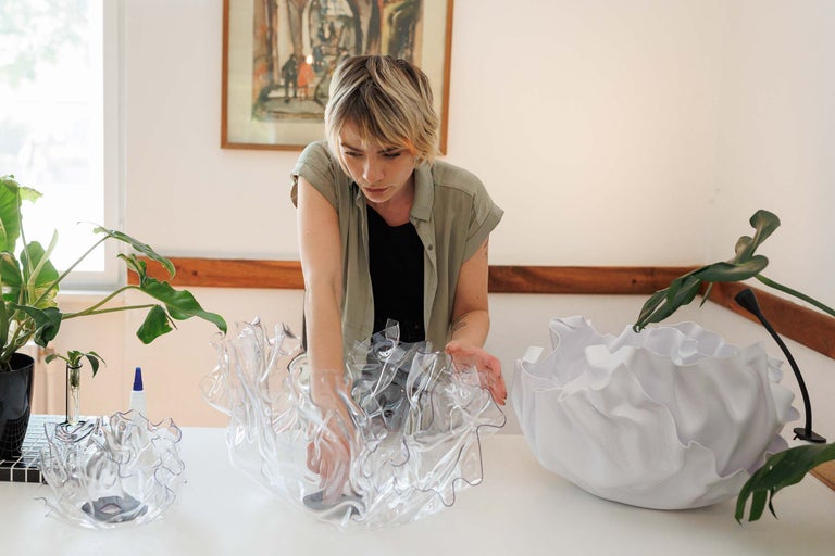 Femeie cu o vază transparentă și albă cu o margine ondulată pe o masă.