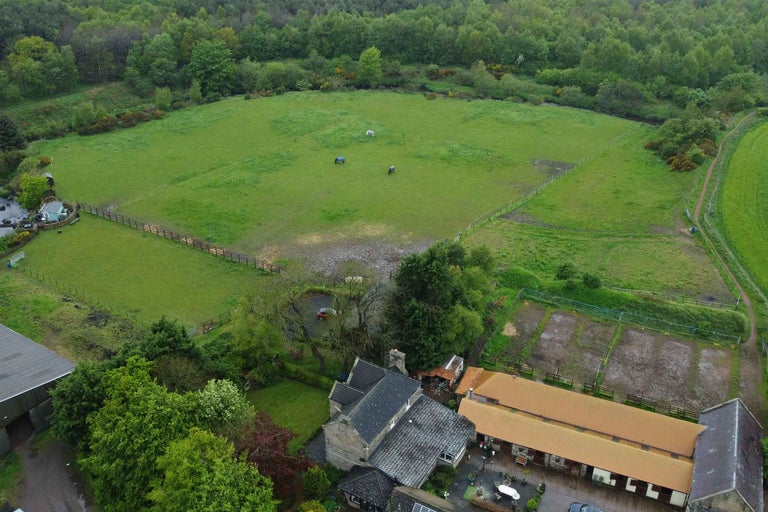 Vedere aeriană a unei proprietăți rurale cu câmpuri, pădure și grajduri.