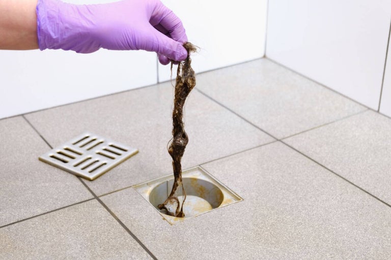 O mână cu mănușă scoate un blocaj dintr-un canal de scurgere.