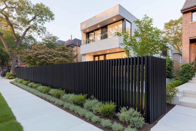 Aspect modern al casei cu gard negru și grădină îngrijită.