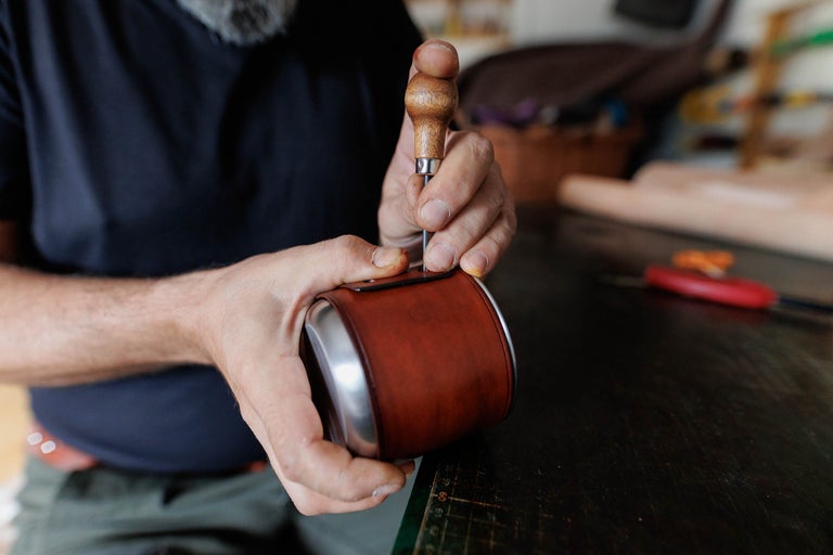 Bărbat prelucrând etui din piele cu ajutorul unei sulă pe bancul de lucru
