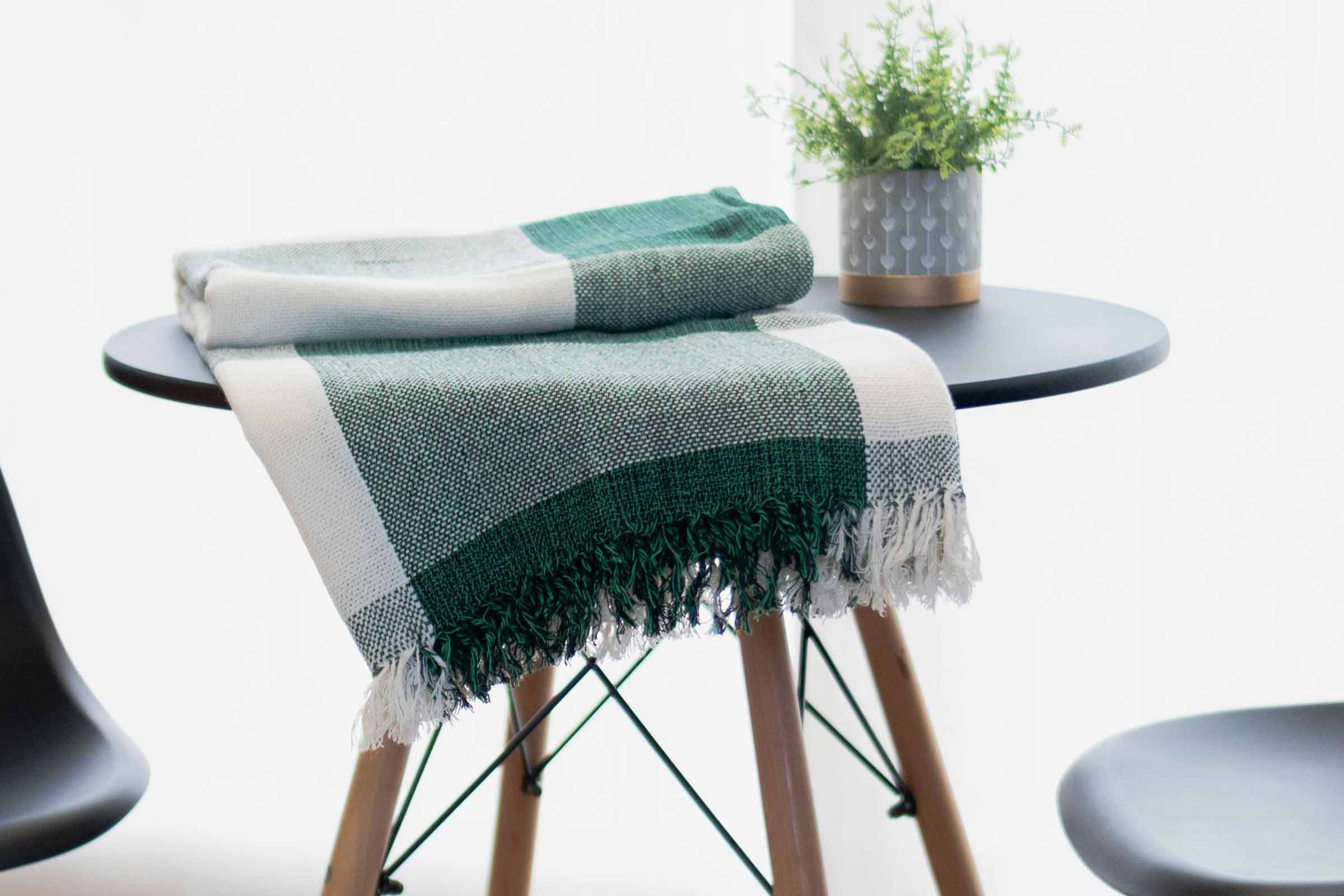 Cuvertură decorativă verde și albă cu franjuri pe o masă
