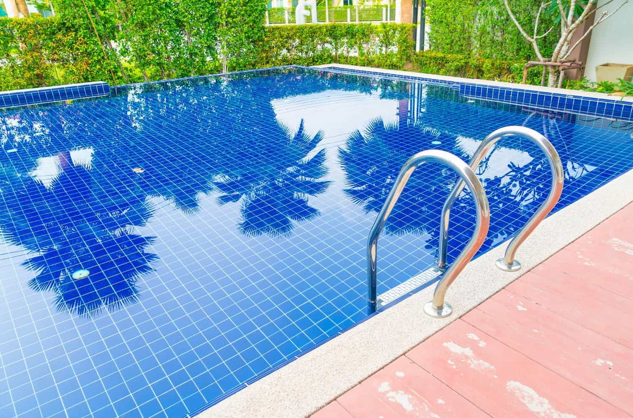 Piscină exterioară cu mozaic albastru, o scară din oțel inoxidabil și o terasă adiacentă.
