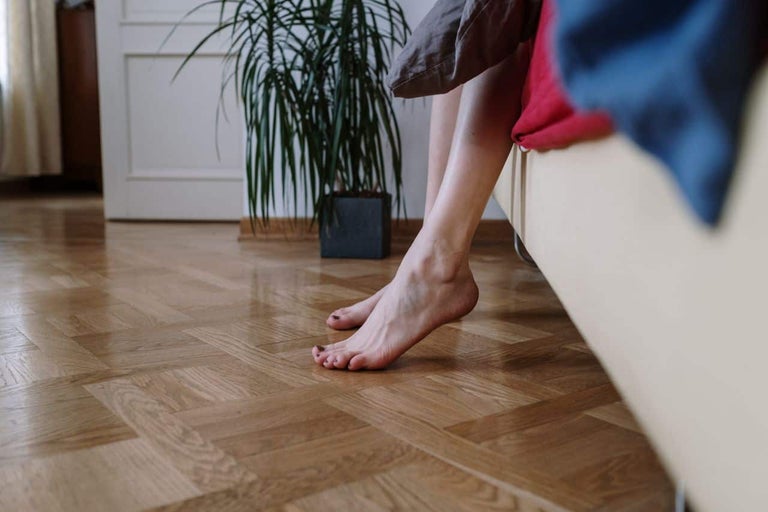 Picioare pe o podea de lemn într-un interior cu parchet în model mozaic și o plantă de apartament în fundal