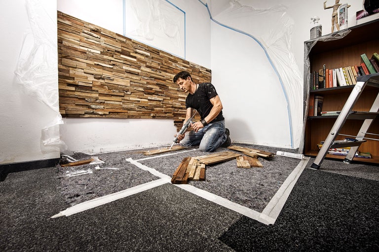 Un bărbat fixează panouri de lemn cu adeziv pe un perete într-o cameră.