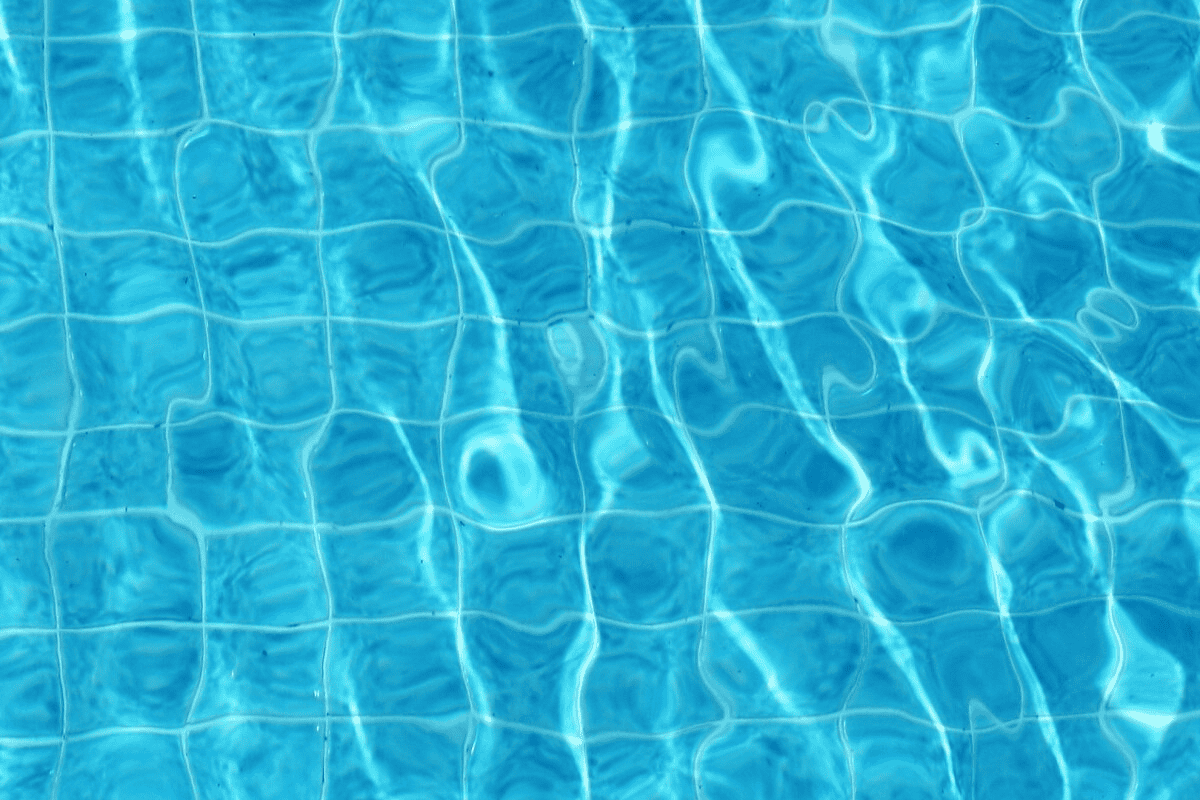 Apă limpede de piscină cu valuri mici și reflexii ale luminii solare peste o rețea de plăci pătrate.