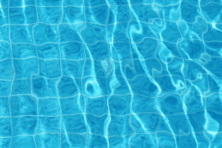 Apă limpede de piscină cu valuri mici și reflexii ale luminii solare peste o rețea de plăci pătrate.