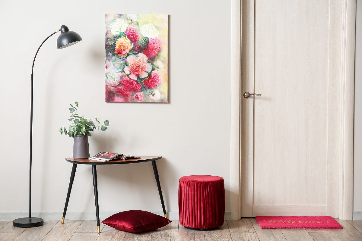 Articole de mobilier într-o cameră: lampă de podea, masă, tablou cu flori, taburet și ușă.