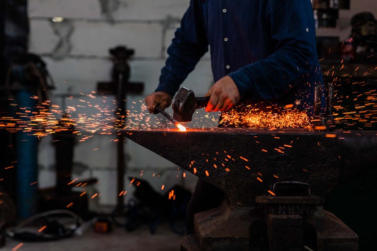 Un fierar prelucrează metalul pe o nicovală cu un ciocan, creând scântei