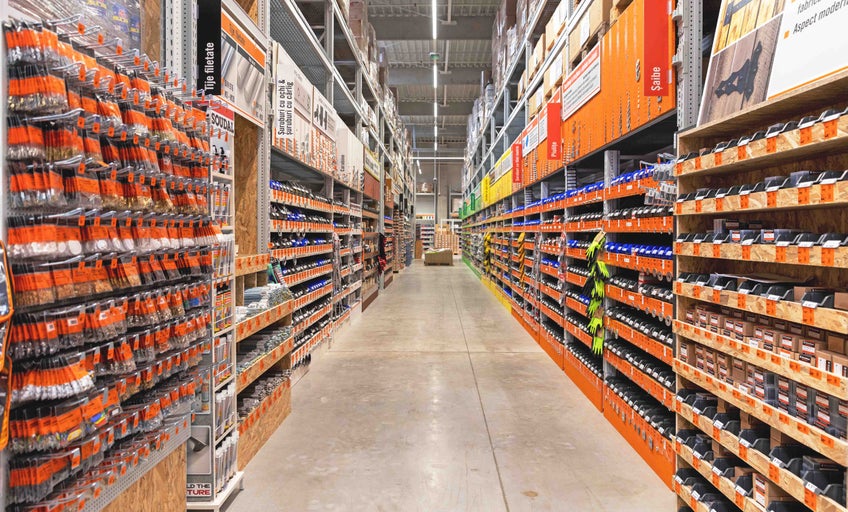Vedere spre culoar în magazinul de bricolaj Hornbach cu rafturi pline cu șuruburi, piulițe și materiale de fixare