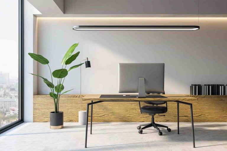 Birou de acasă modern cu masă din lemn, scaun de birou negru, plantă mare de apartament și pendul LED subțire. Spațiu de lucru luminos.