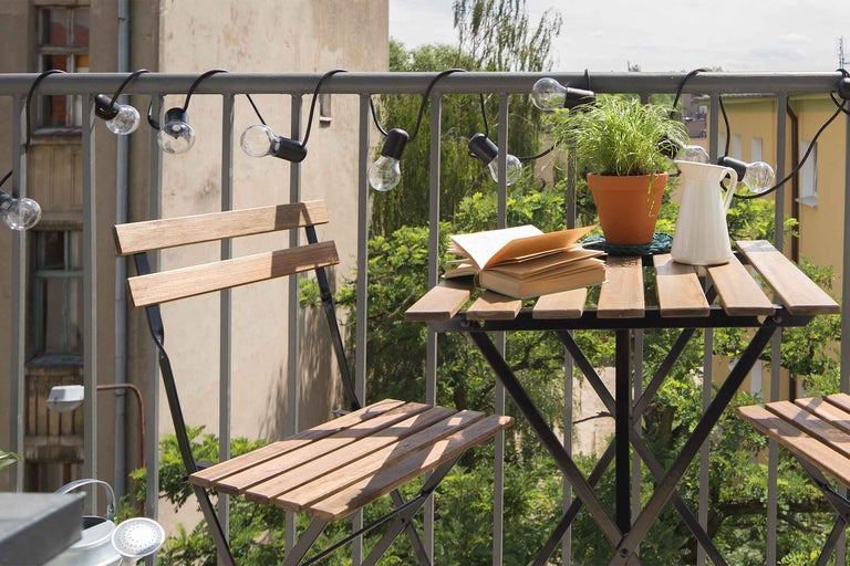 Balcon cu mobilier din lemn, lanț de lumini, plantă la ghiveci, carte și ulcior