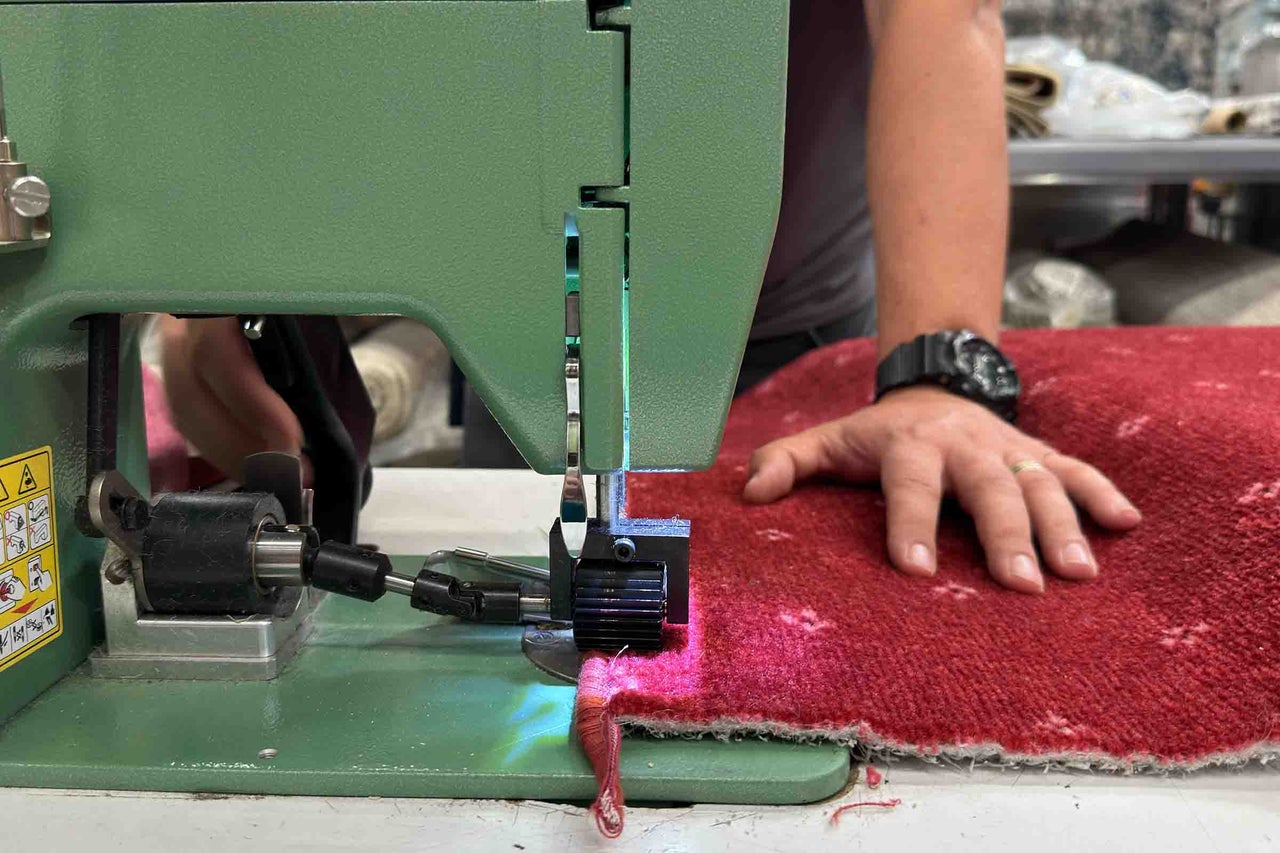 Prim-plan cu o mașină de bordurat covoare care lucrează la un covor.