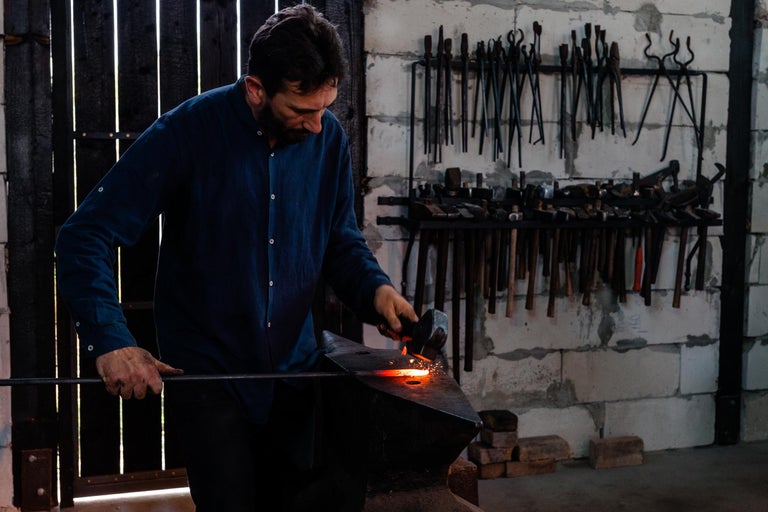 Fierar prelucrează metal incandescent pe o nicovală cu un ciocan.