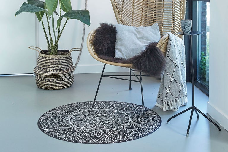 Imagine de ansamblu a unei camere cu covor rotund, scaun de ratan, măsuță laterală, plantă de interior și accesorii pentru casă