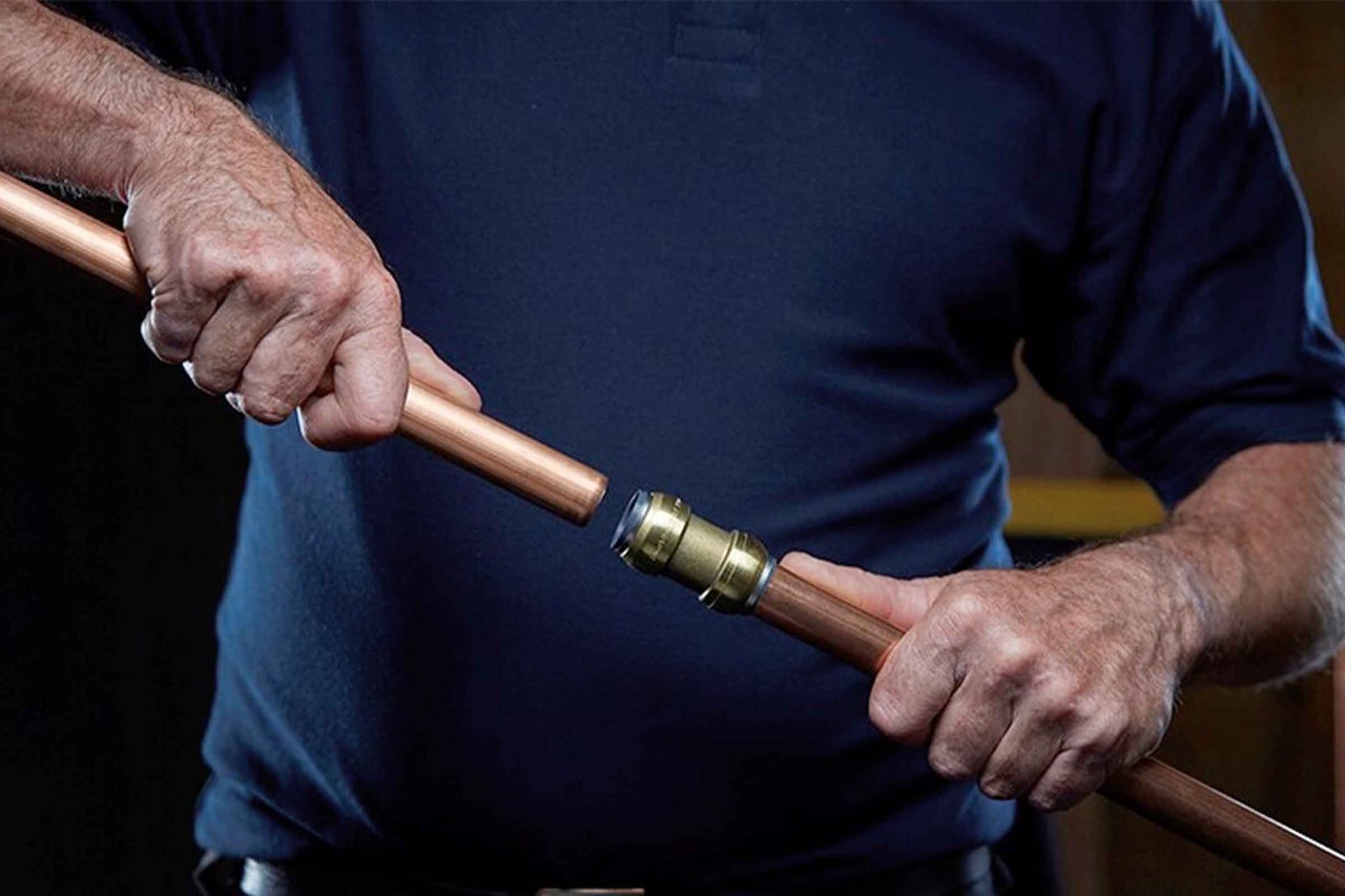 O persoană îmbină două țevi de cupru cu un racord rapid din alamă.