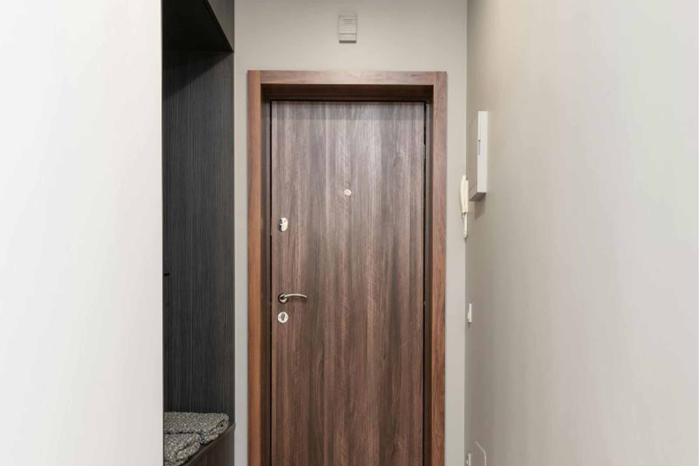 Fotografie de interior cu o ușă de lemn cu feronerie și vizor într-un hol