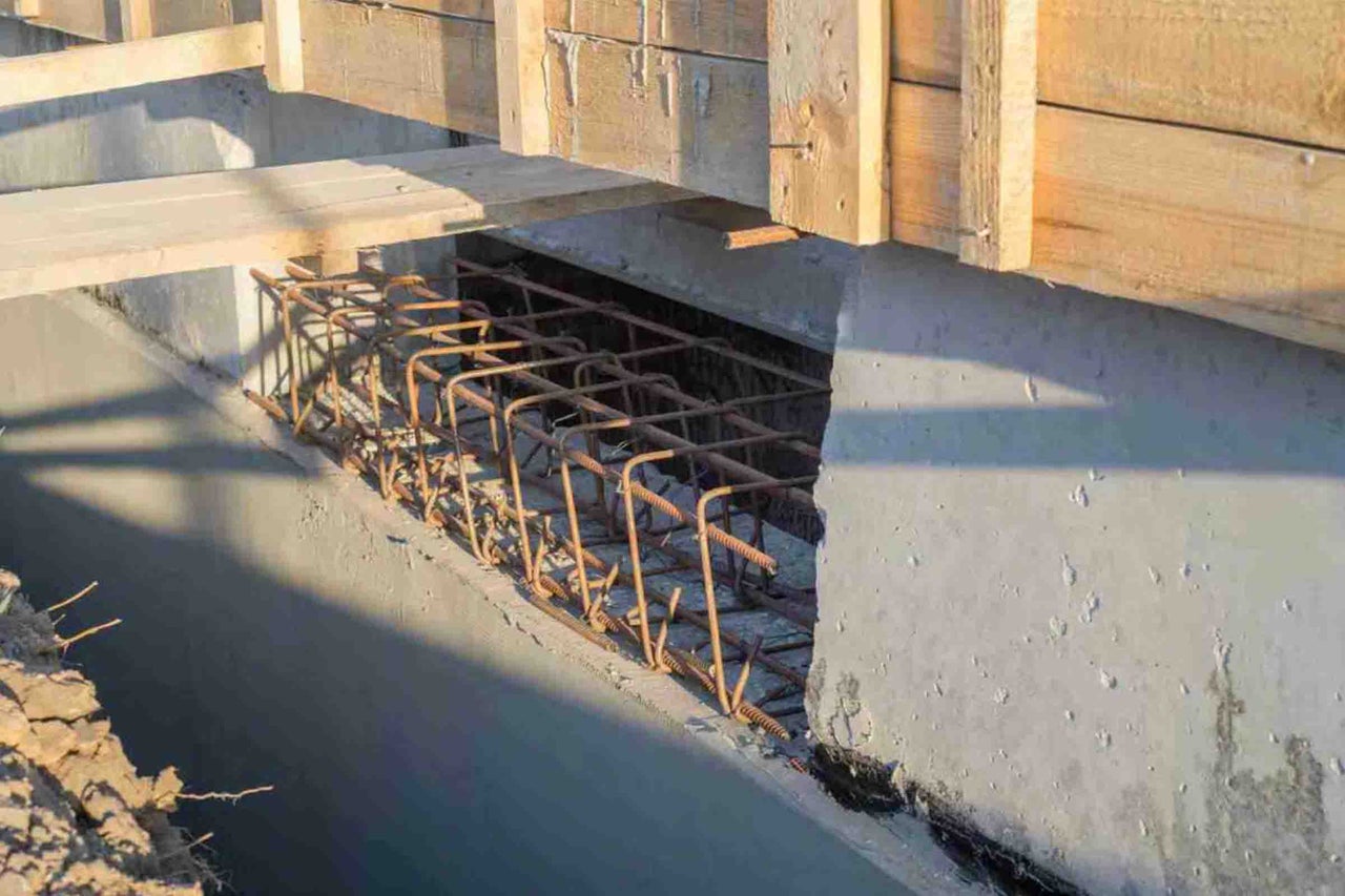 Fundație de beton cu armătură de oțel într-un șanț cu cofraj de lemn în partea superioară.