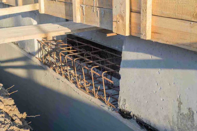Fundație de beton cu armătură de oțel într-un șanț cu cofraj de lemn în partea superioară.