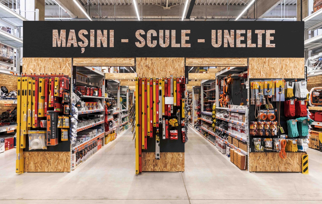 Vedere a culoarului în magazinul de bricolaj Hornbach cu rafturi pline cu scule și mașini.
