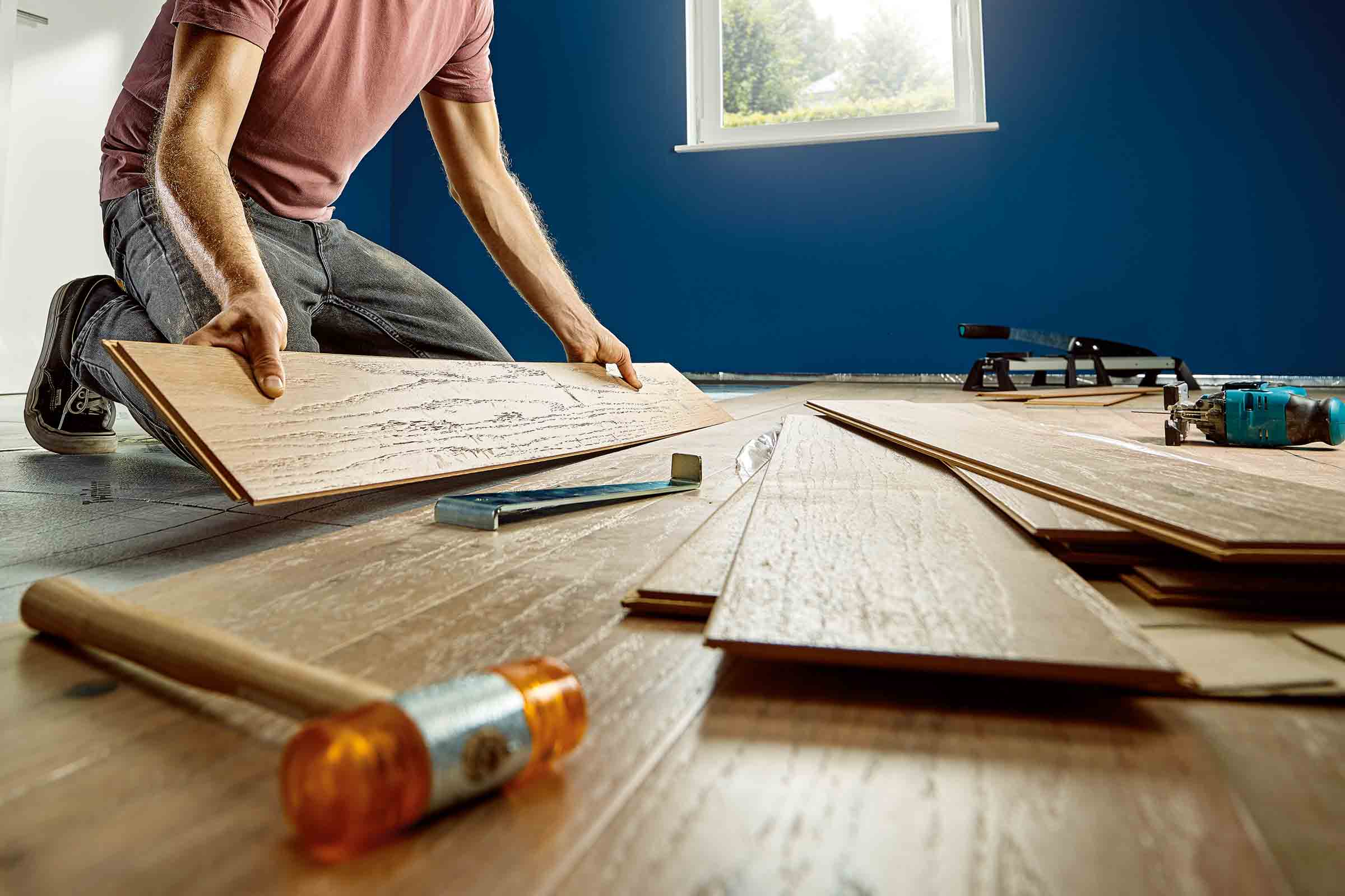 Un bărbat instalează parchet laminat cu unelte într-o cameră.