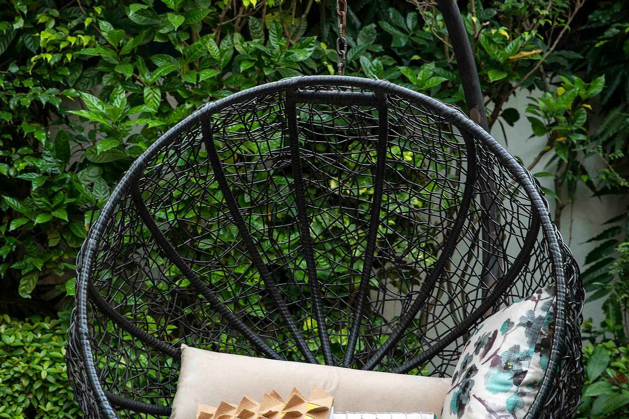 Prim-plan cu un scaun suspendat din ratan cu perne în grădină