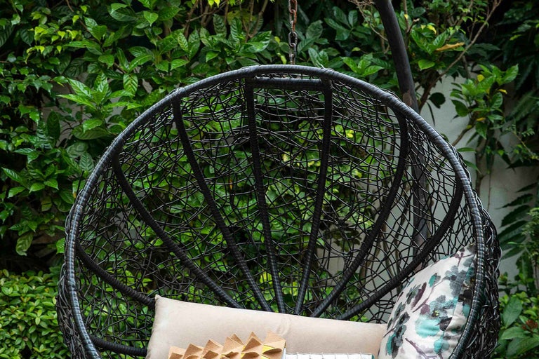 Prim-plan cu un scaun suspendat din ratan cu perne în grădină