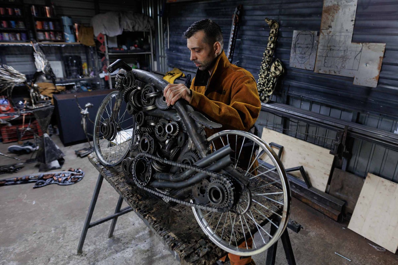 Operă de artă metalică a unei biciclete cu un bărbat în atelier.