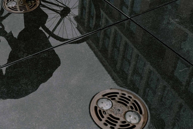 Reflecția unei persoane cu bicicletă pe podea placată cu rigolă de scurgere