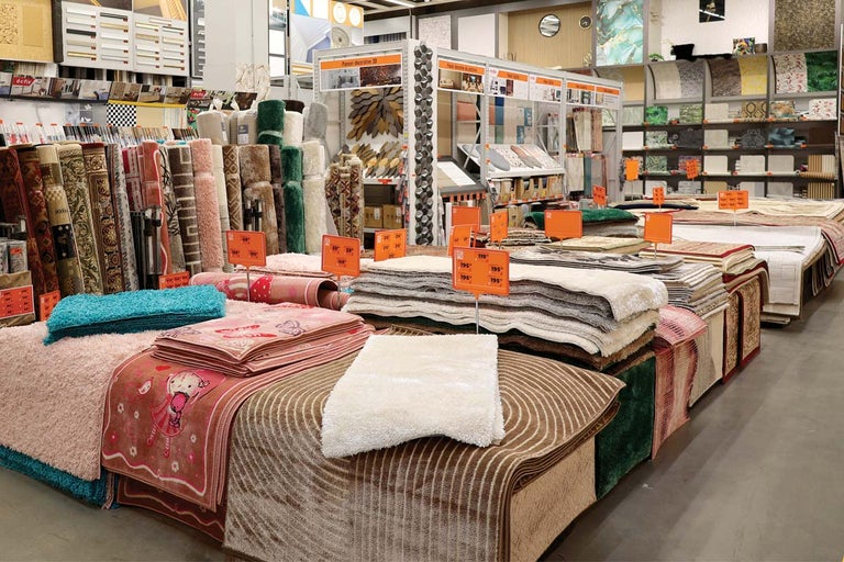 Expoziție cu diverse covoare și traverse într-un magazin de bricolaj.