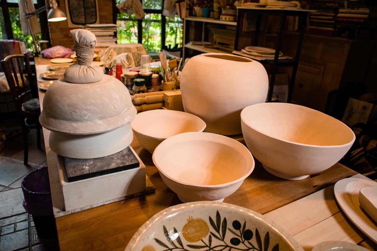 Diverse produse ceramice brute, cum ar fi boluri și vaze, într-un atelier pe o masă.