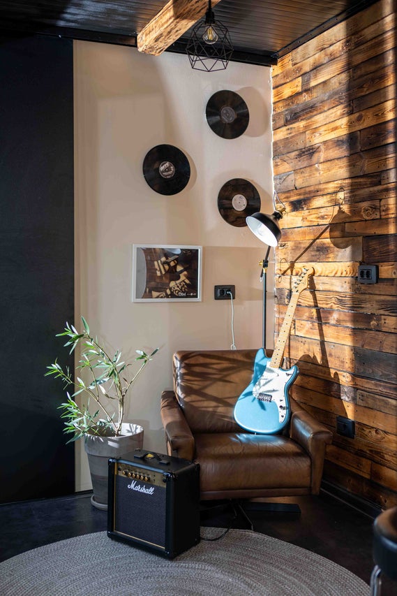 Zona de zi in stil industrial cu fotoliu din piele, chitara electrica, amplificator Marshall, lambriu din lemn si discuri decorative pe perete.