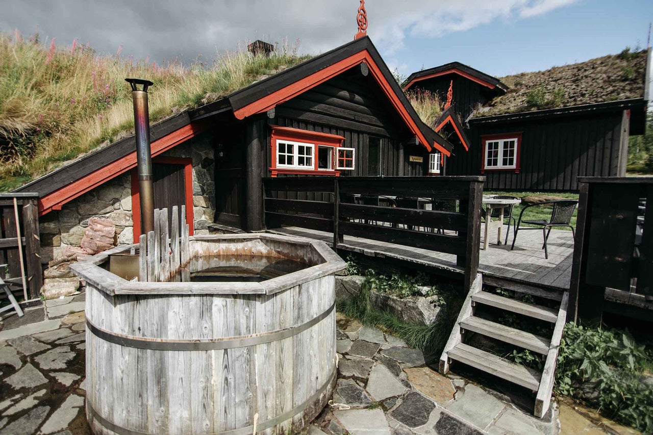 Exterior cu cadă fierbinte din lemn, cabană din lemn cu acoperiș din iarbă și terasă de piatră