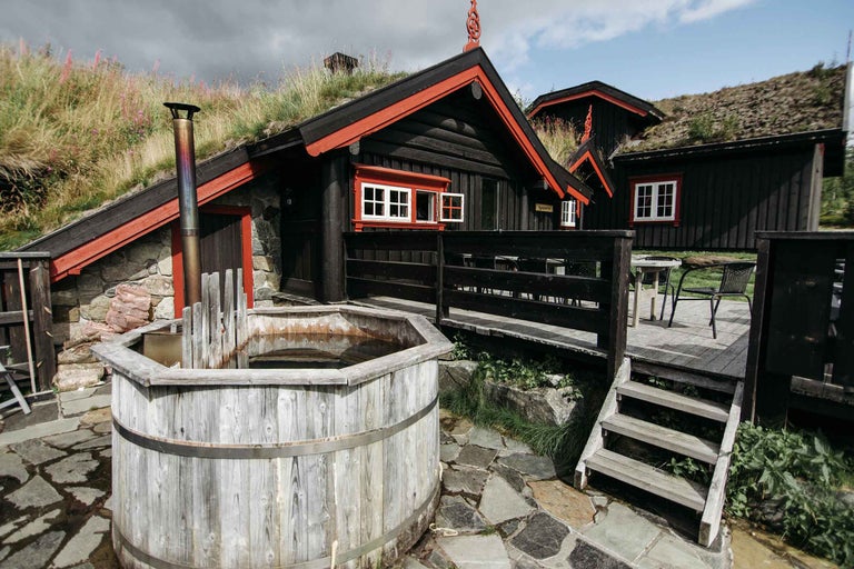 Exterior cu cadă fierbinte din lemn, cabană din lemn cu acoperiș din iarbă și terasă de piatră