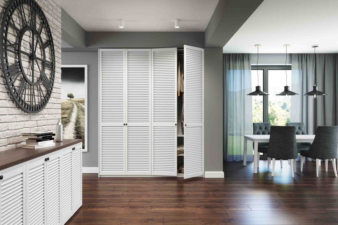 Cameră de zi modernă cu uși cu lamele albe pentru dulapuri încorporate și o comodă, podea din lemn închis, ceas de perete mare și zonă de luat masa.