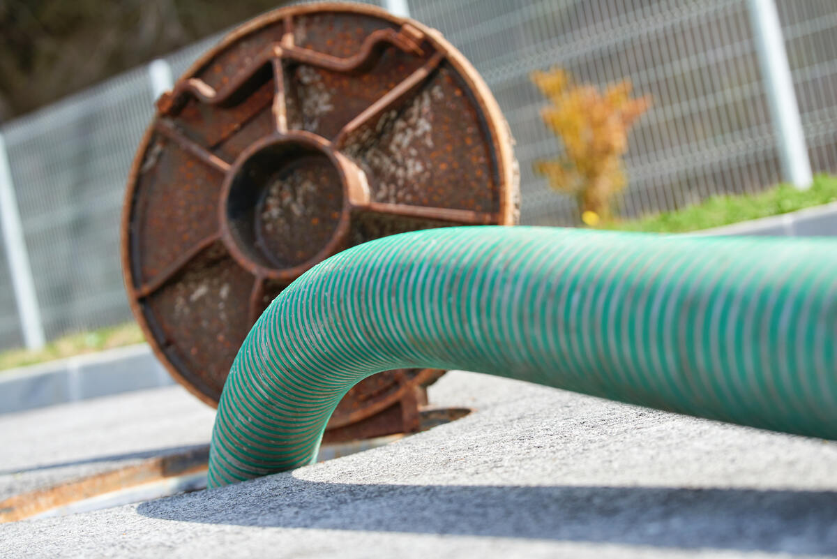 Furtun verde de grădină pe suprafață de beton cu bobină ruginită în fundal.