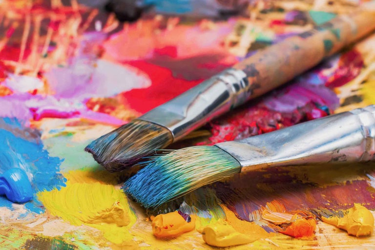 Două pensule stau pe o paletă de vopsea cu tuburi de vopsea