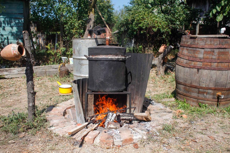 Scenă în aer liber cu cuptor pe lemne, oală mare, butoi și ulcior de faianță.