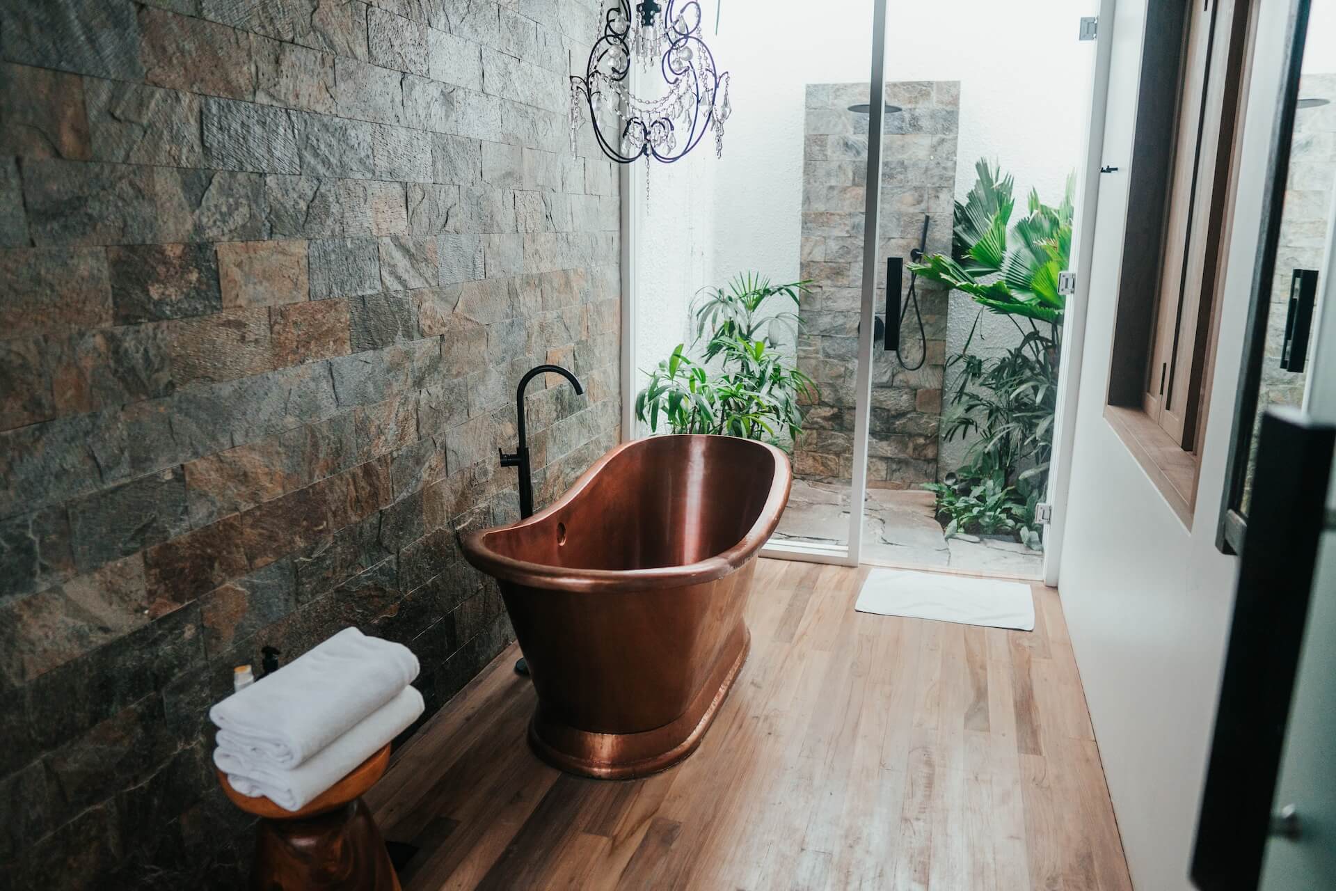 Baie cu cadă freestanding, perete de piatră și duș