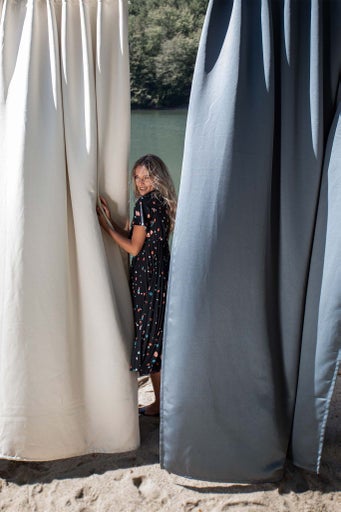 Femeie pozând între două perdele de duș în aer liber