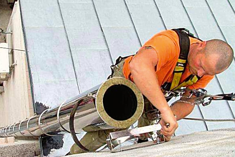 Un muncitor instalează un sistem de coș de fum din oțel inoxidabil pe un acoperiș.