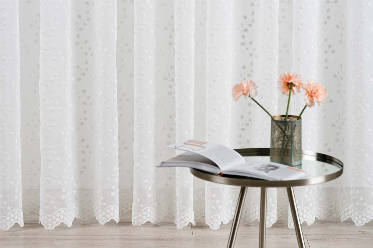 Cortină albă din voal cu model floral lângă măsuța laterală