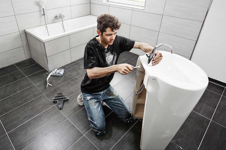 Instalator montează lavoarul în baie.
