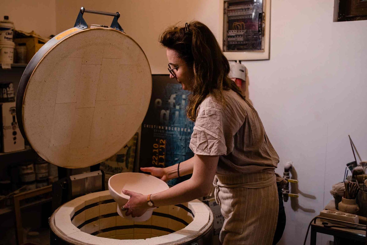 Femeie scoate un vas ceramic din cuptorul ceramic