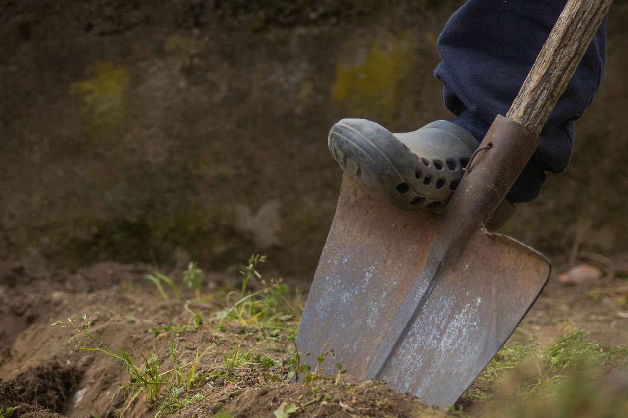 O persoană folosește un hârleț în grădină cu un picior