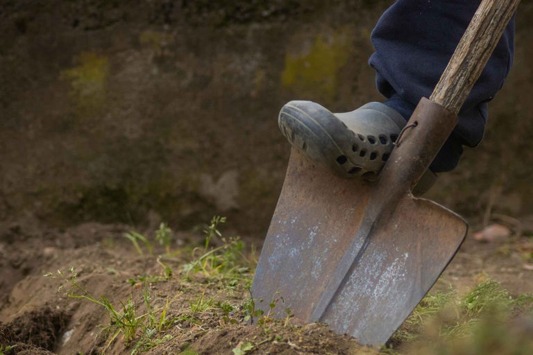O persoană folosește un hârleț în grădină cu un picior